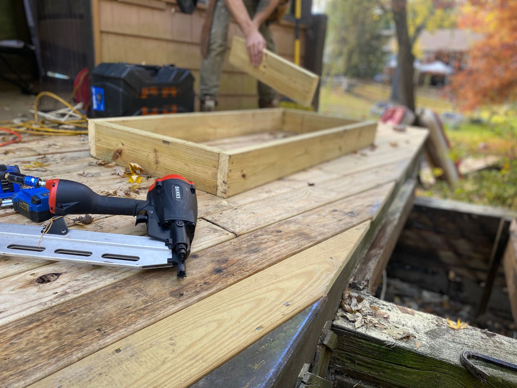 A pneumatic nail gun resting on new wooden deck boards during outdoor terrace construction.
