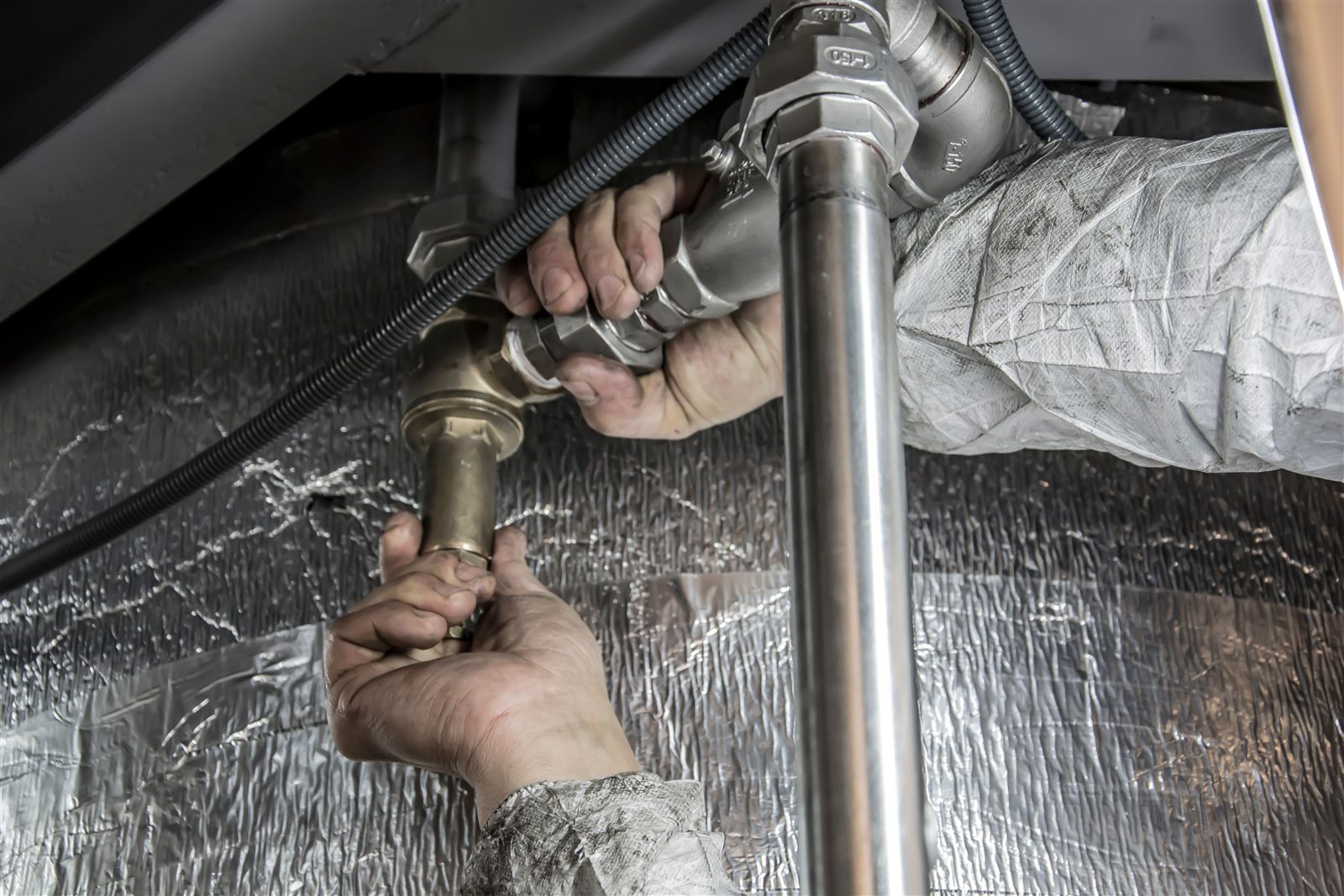 Plumber’s hands tightening metal pipe fittings during a repair