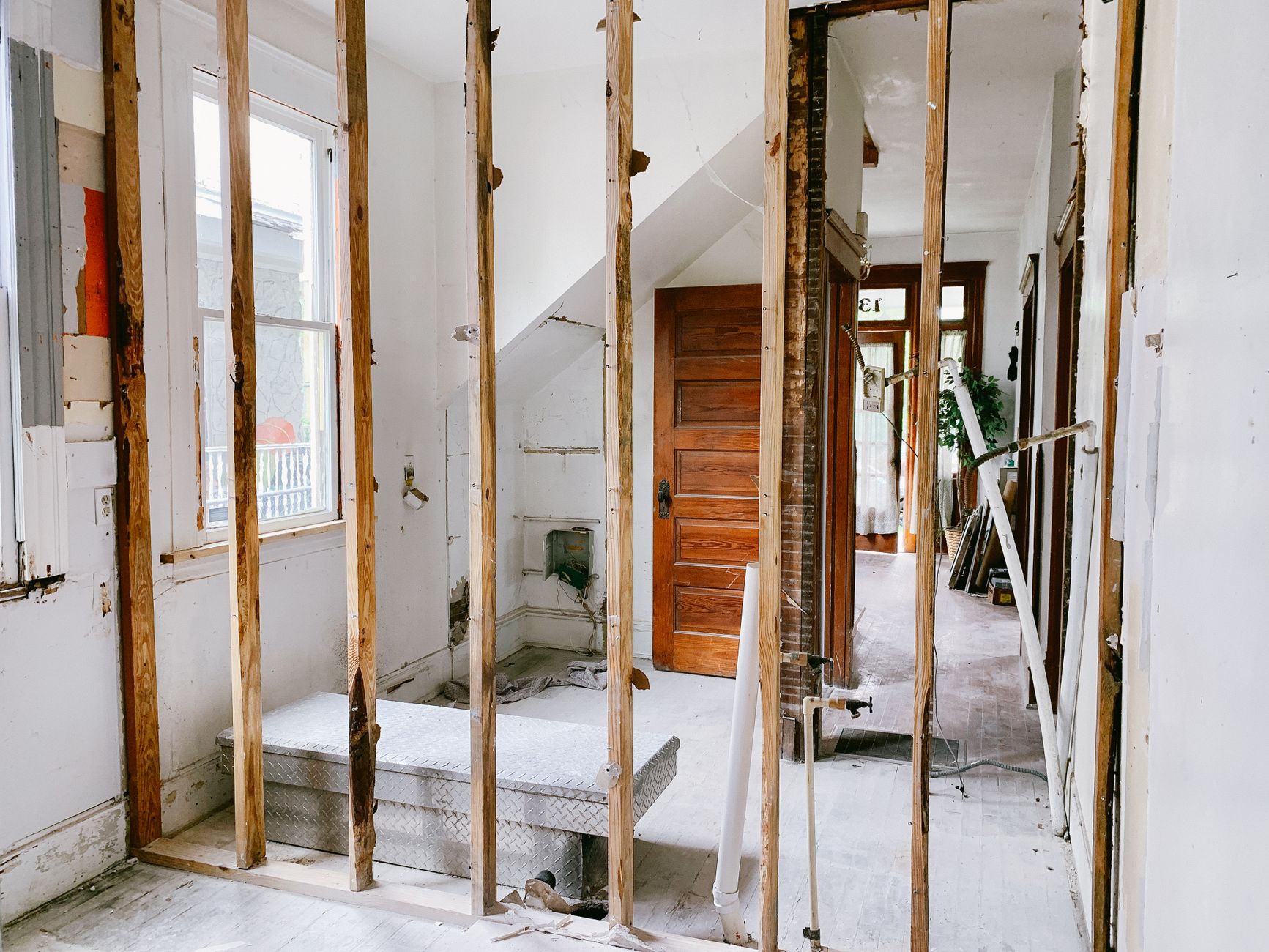 Exposed stud wall in an older home mid-renovation, revealing original framing and wood door