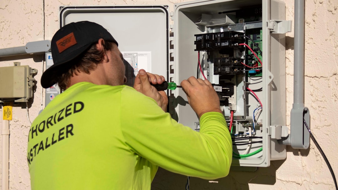 A licensed installer working on an open residential electrical panel and meter enclosure mounted on exterior siding