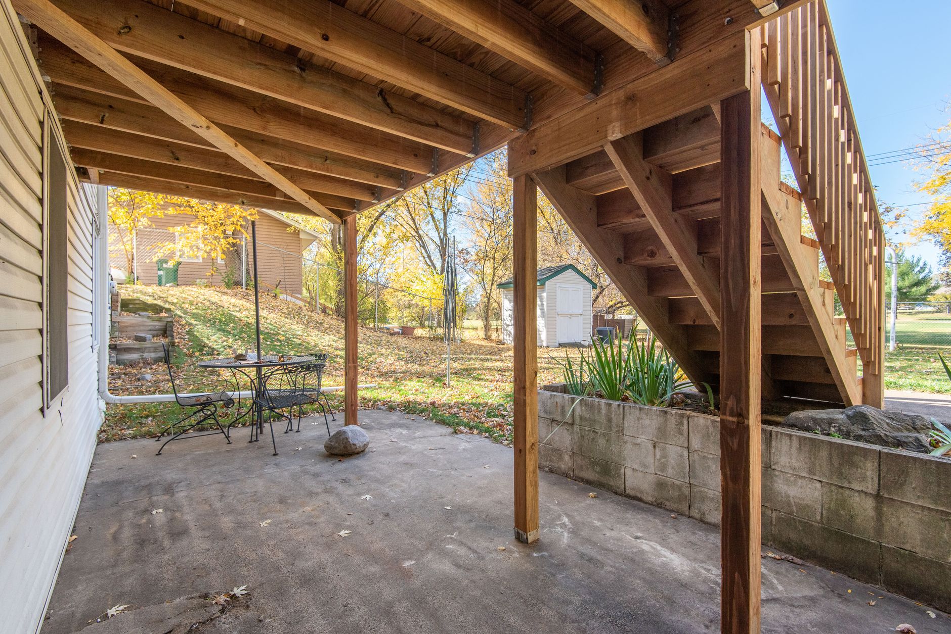 Wooden outdoor stairs leading from a house down to a backyard patio in autumn.