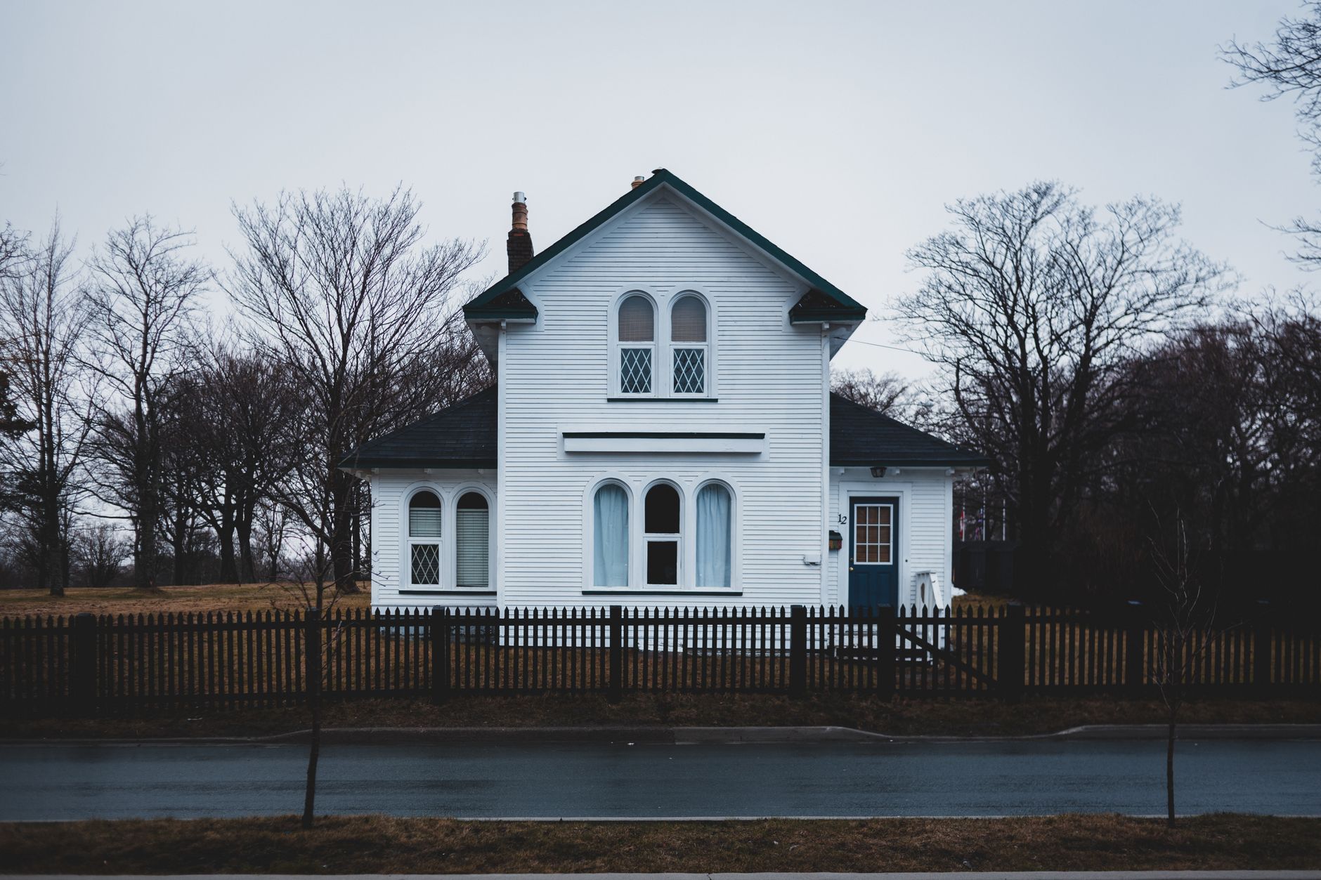 A white house with bare winter trees and a wet street on an overcast fall day.