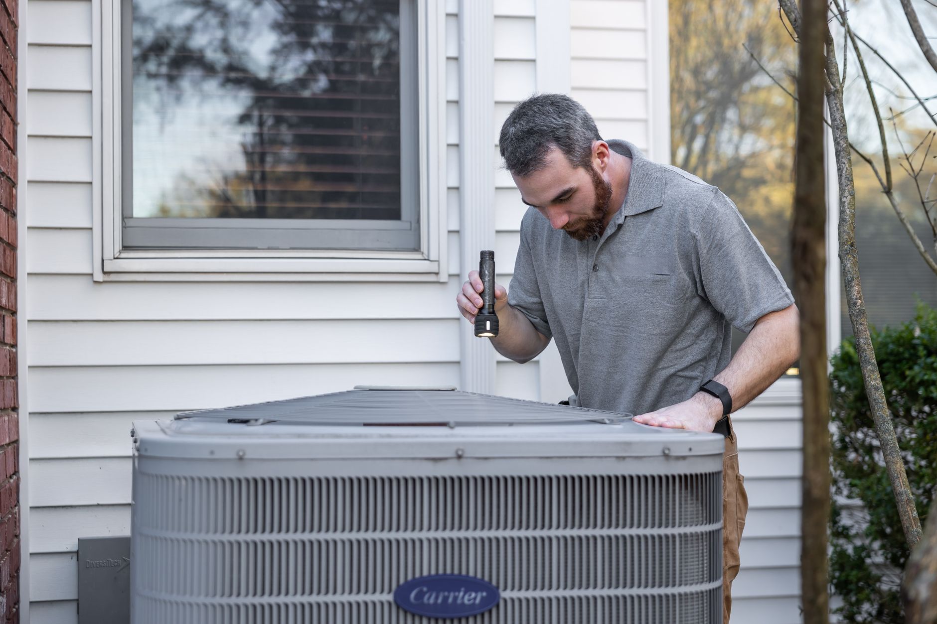 A technician inspects an outdoor HVAC/heat pump unit as part of seasonal maintenance.