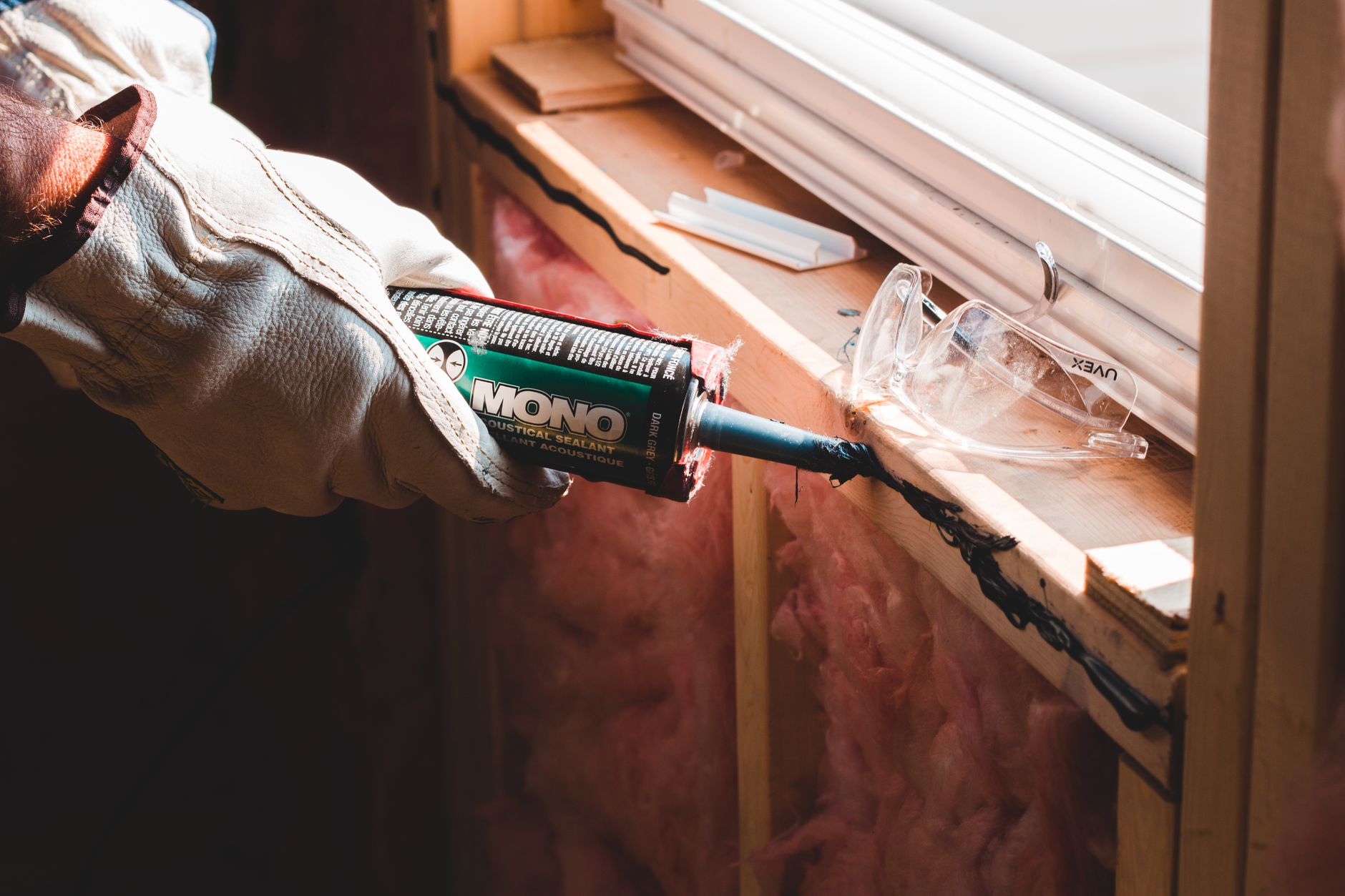 A gloved hand applies caulk along a window seam during exterior sealing work.