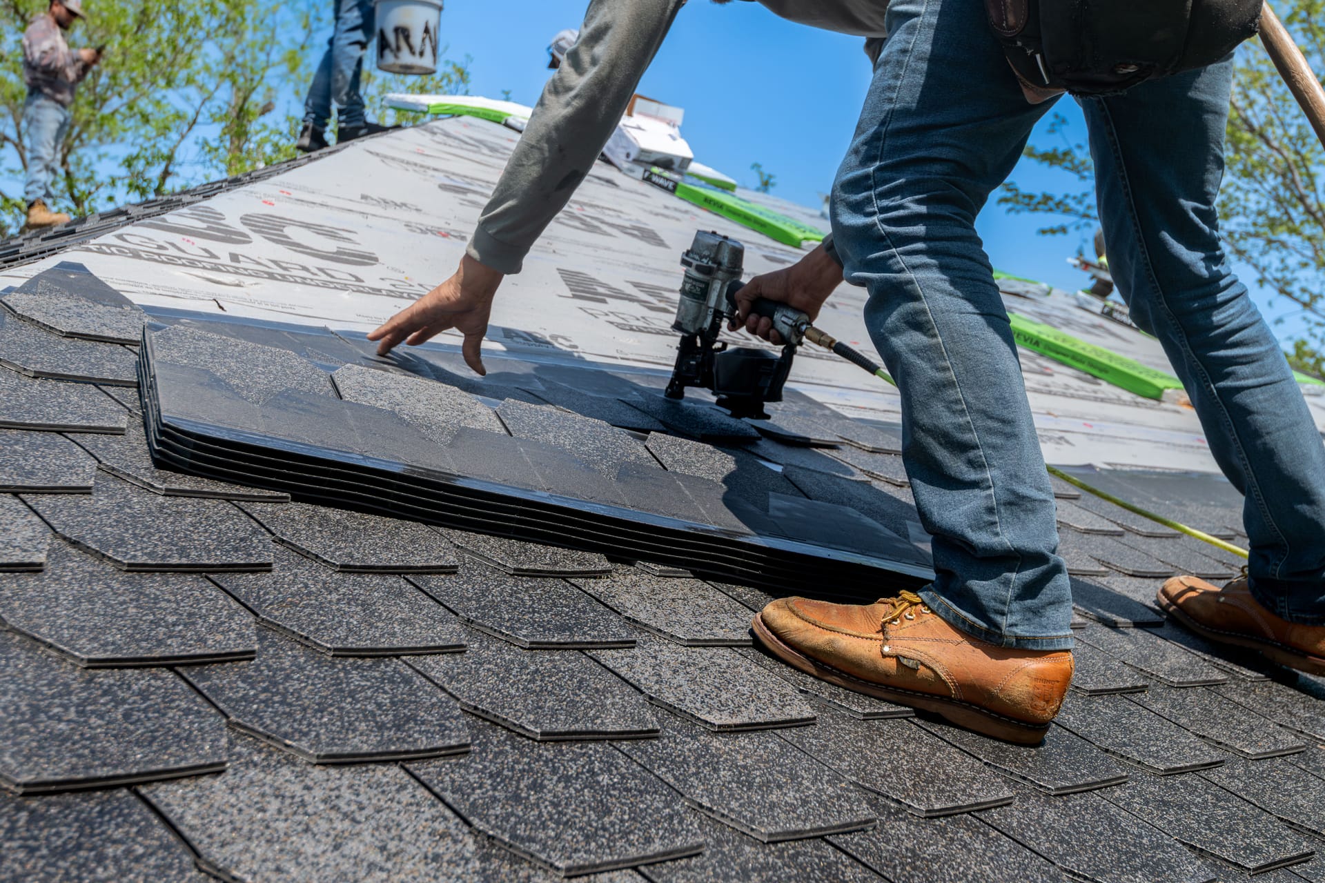 Roofer using a nail gun to install new asphalt shingles on a residential roof