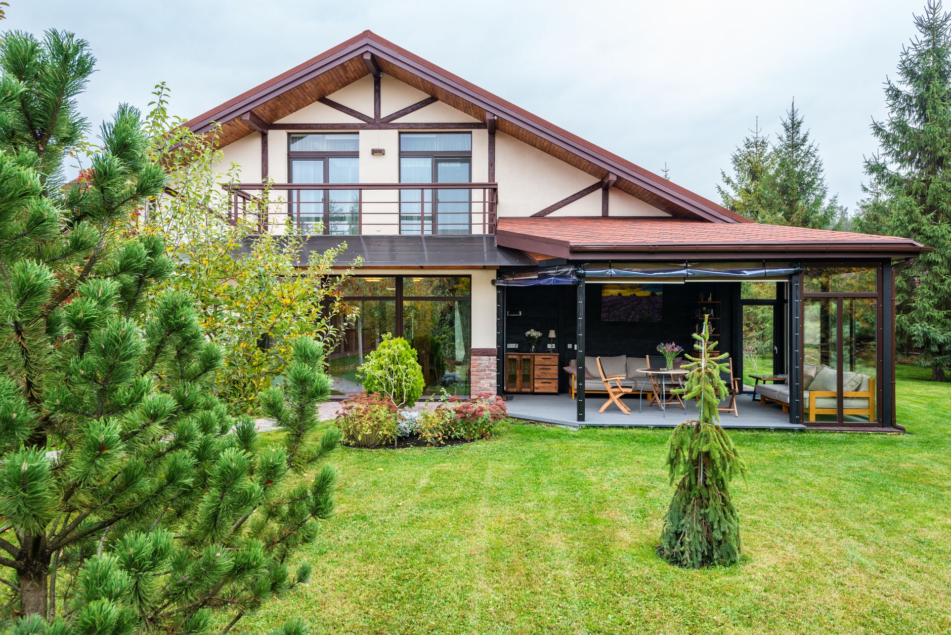 A bright modern house exterior with warm wood siding, a second-story balcony, and a green yard in summer.