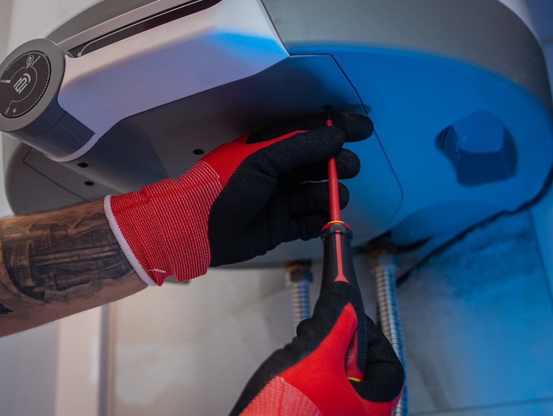 Technician wearing gloves using a screwdriver to service a compact wall-mounted tankless water heater unit