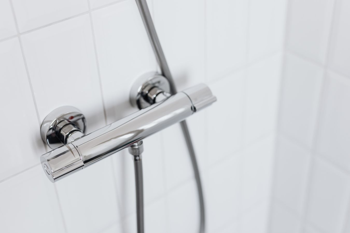 Modern chrome shower faucet on a clean white tiled bathroom wall